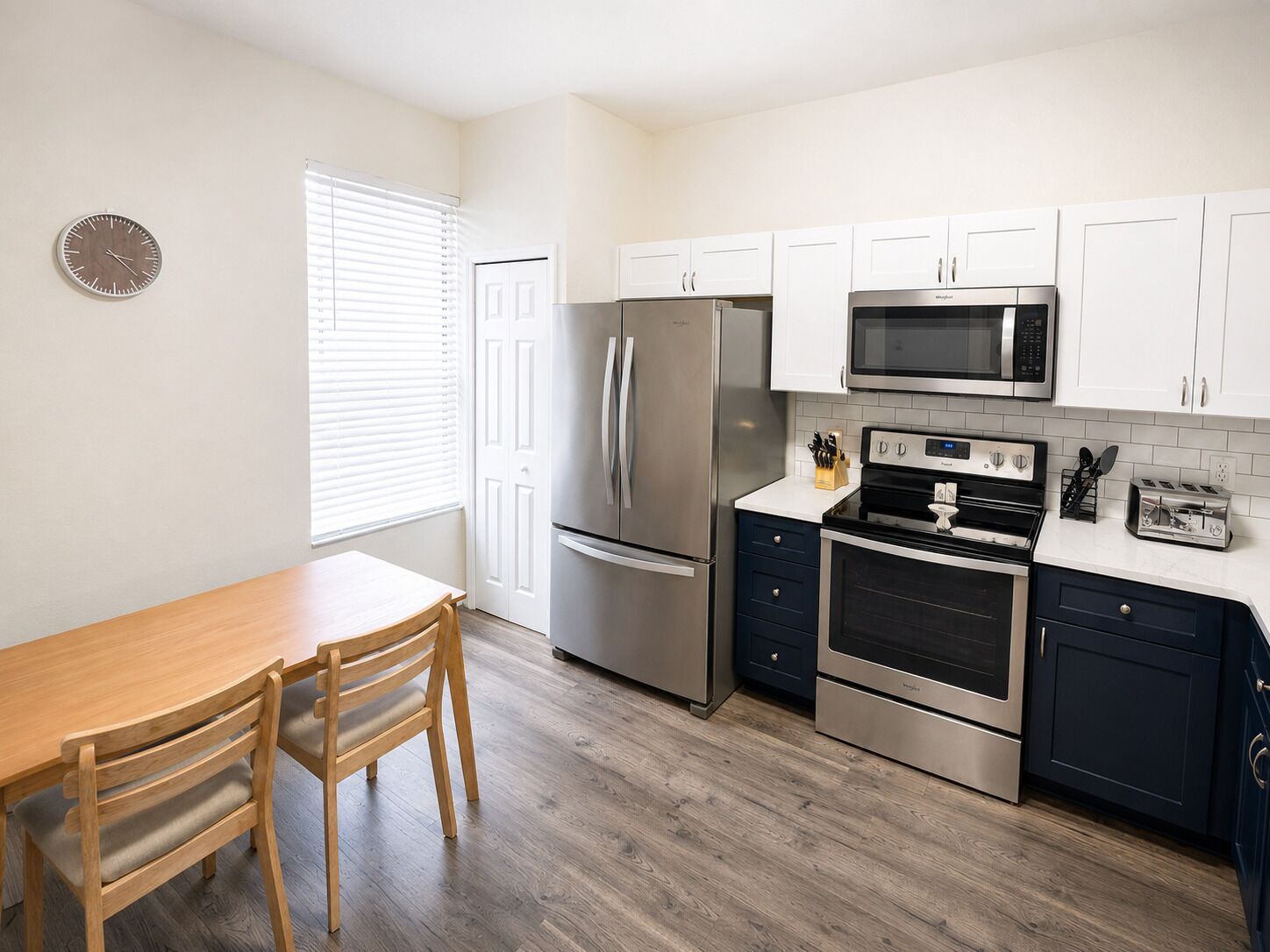 A modern kitchen with stainless steel appliances, white cabinets, and a wooden dining table.