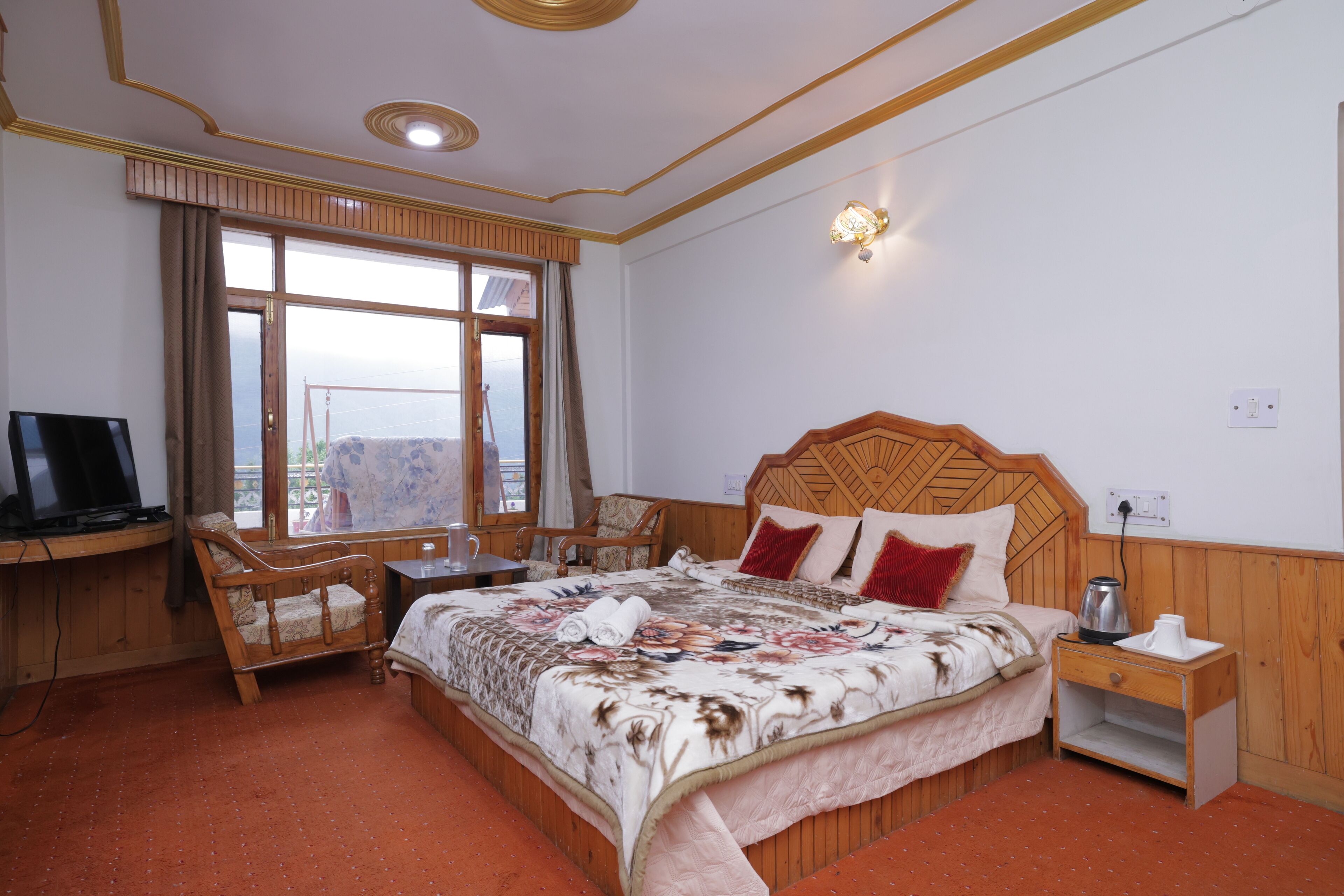 A bedroom with a large bed, wooden headboard, a desk with a computer, and a window with curtains.