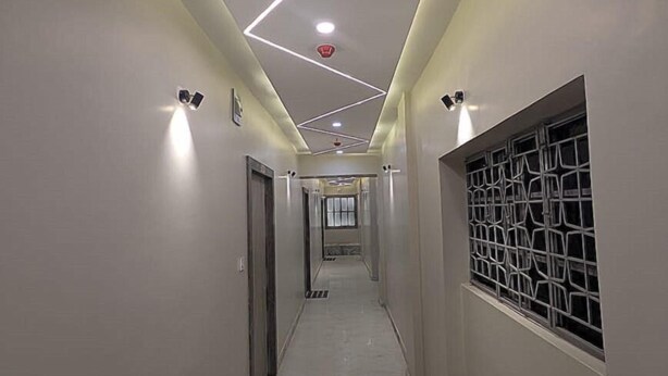 Un pasillo moderno con iluminación empotrada, un acceso central y una ventana con celosía metálica a la derecha.