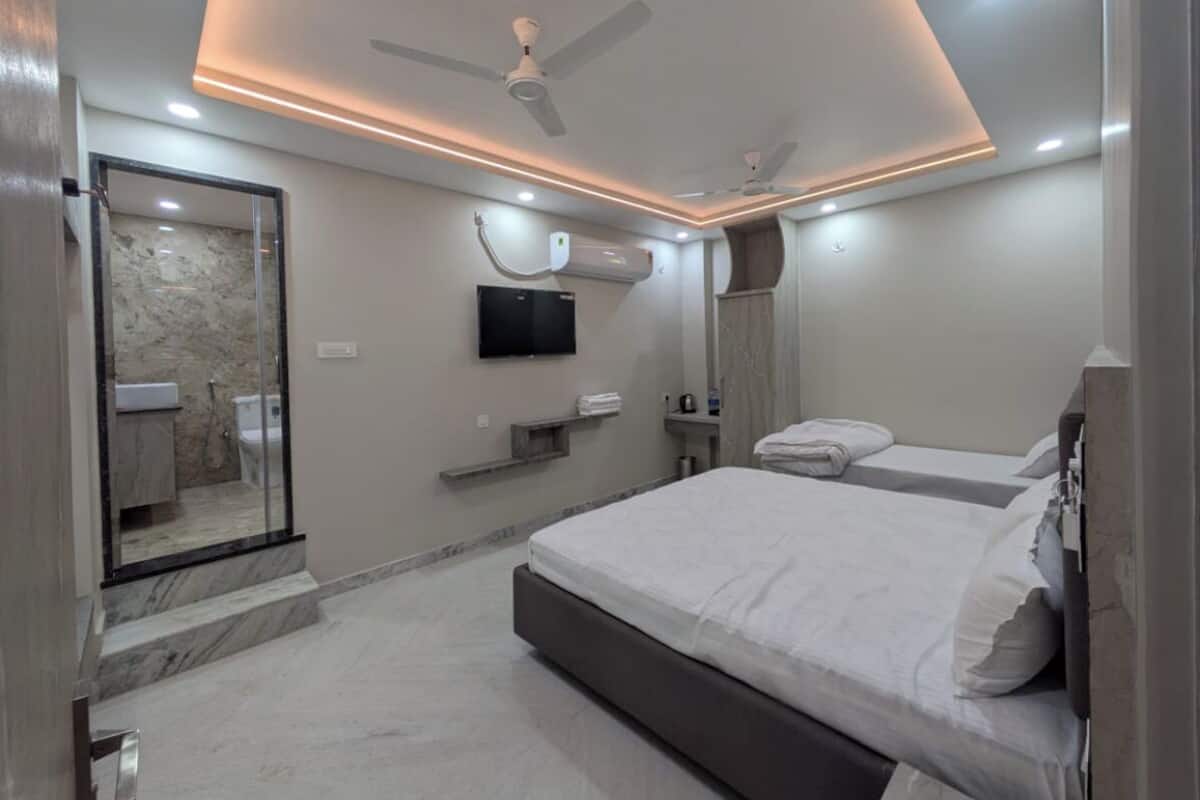 A modern bedroom with a large bed, a ceiling fan, a mounted TV, and a bathroom with a marble wall and glass shower enclosure.