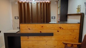 Una recepción con mostrador de madera y superficie negra, una cortina marrón y una silla con tapicería marrón.