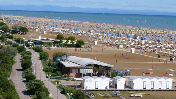A beach with numerous umbrellas and tents, a parking area, and a building with a sign. - Cometa 3 in Bibione With 2 Bedrooms and 2 Bathrooms (San Michele al Tagliamento)