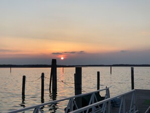 Un atardecer sobre un lago tranquilo con un muelle y postes de madera.