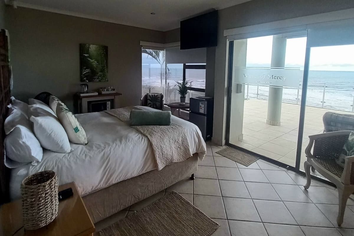 A bedroom with a large bed, a TV, and a view of the beach through a sliding door.