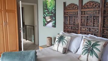 A bedroom with a bed, a wooden headboard, a painting of a forest, and a door leading to another room.