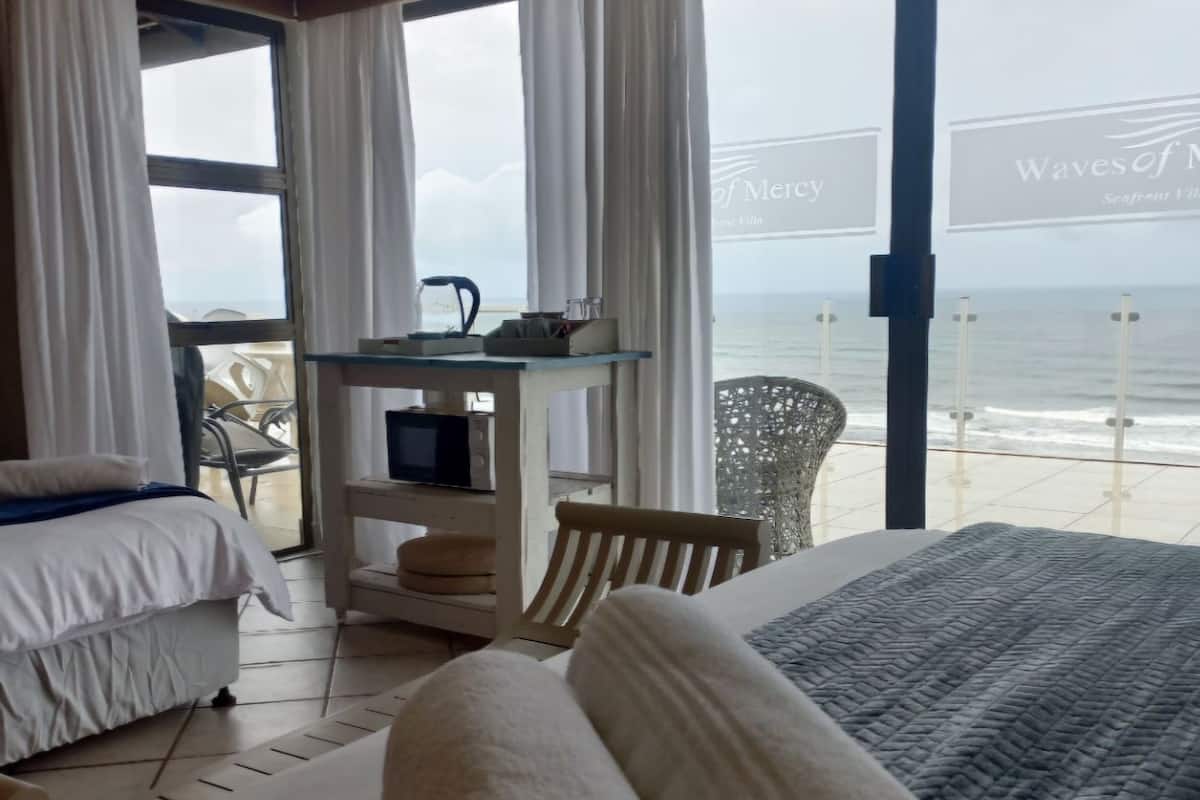 A hotel room with a bed, a TV, a desk, and a view of the sea.