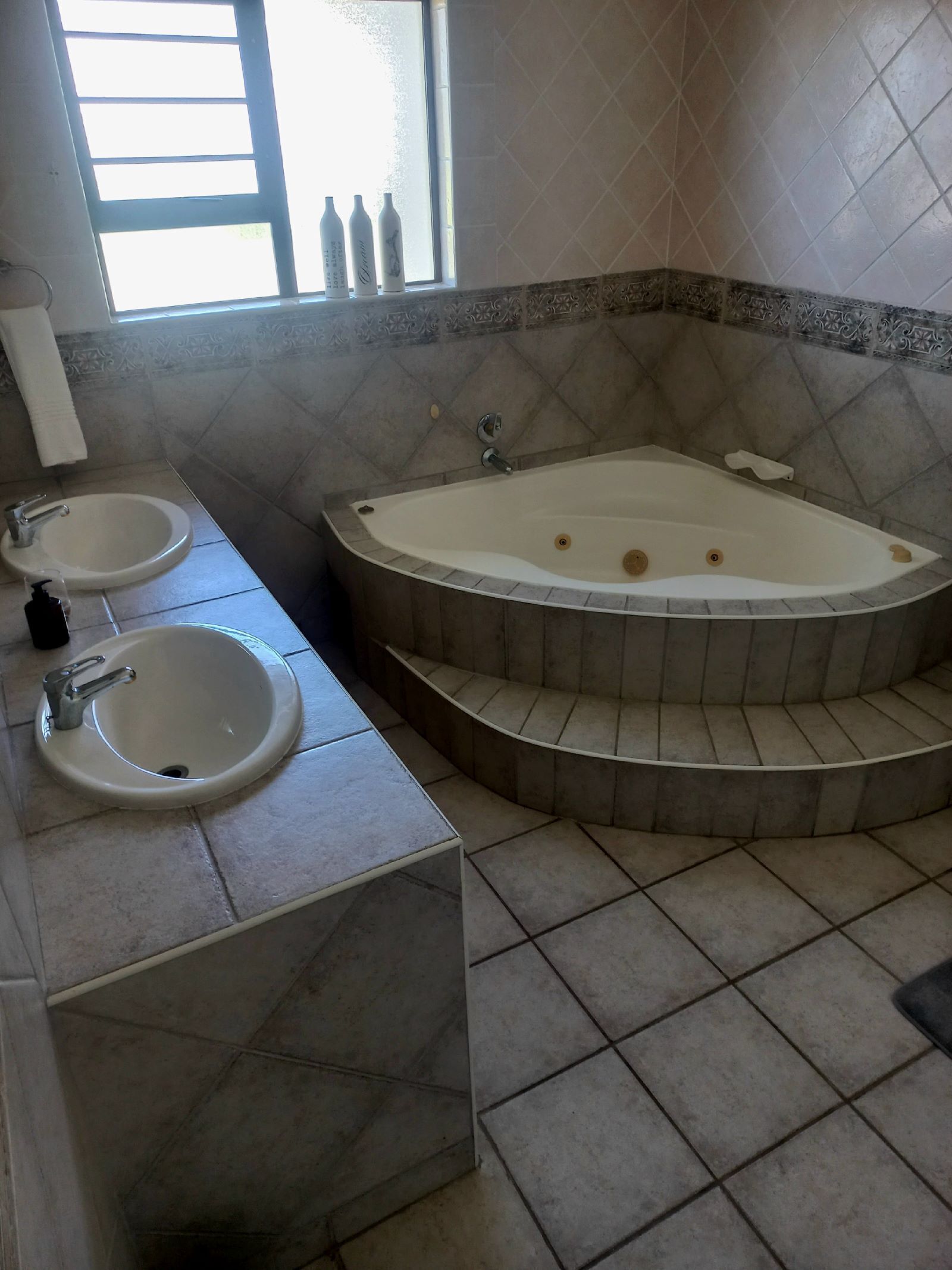 A bathroom with two sinks, a bathtub, and a window with bottles on the sill.