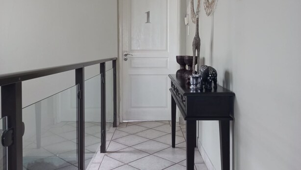 Een gang met glazen balustrade, een deur met nummer 1 en een console tafel met decoratieve objecten.
