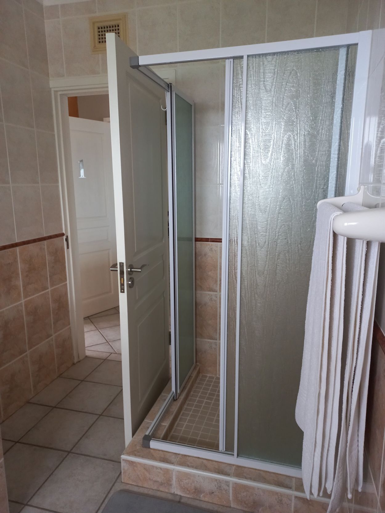 Un área de ducha con puerta de vidrio, un perchero y suelo de baldosas.