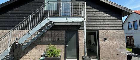 Un edificio de dos plantas con balcón, escaleras y una puerta que da a un espacio interior.