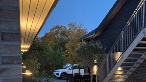 An outdoor patio area with wicker furniture, a white car, and a staircase leading to an upper level. - 6 person modern apartment with style and comfort (Lejre)