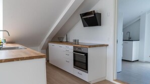 A modern kitchen with white cabinetry, a wooden countertop, and a built-in oven. - 6 person modern apartment with style and comfort (Lejre)