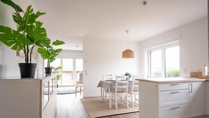Una cocina moderna con armarios blancos, un comedor con mesa y sillas, y ventanas amplias.