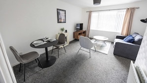 A compact living space with a dining area, a sofa, a TV, and a window with curtains.