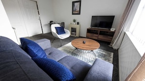 A living room with a grey sofa, a blue pillow, a wooden coffee table, a TV, and a fireplace.