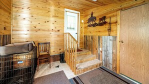 A wooden interior with a staircase, a dog crate, a chair, and a door with a horse and dog mural.