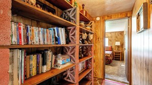 A cozy room with a wooden bookshelf filled with books and decorative items, a small table with a lamp, and a door leading to another room.