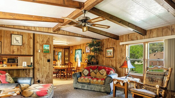 A rustic interior with wooden walls, a dining area, and a cozy seating arrangement including a sofa and a chair.