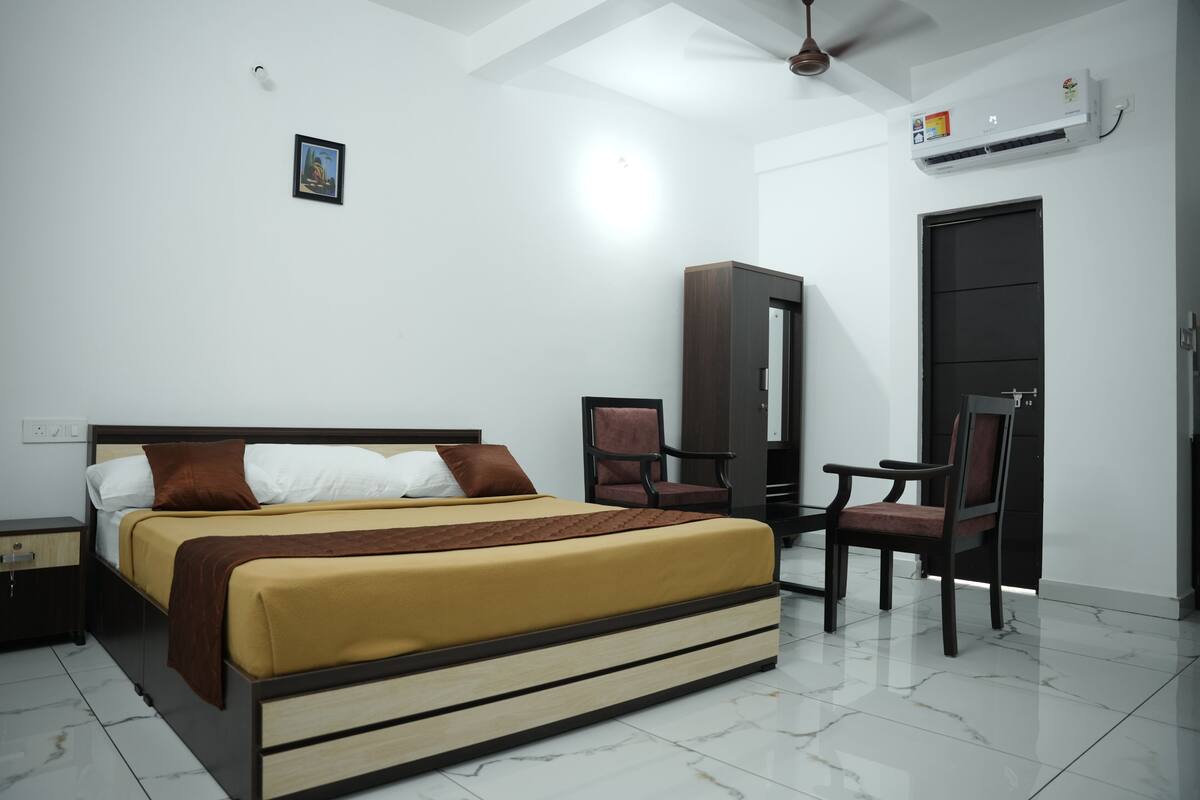 A modern bedroom with a bed, a chair, a wardrobe, and an air conditioning unit.