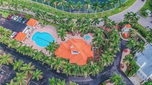 An aerial view of a resort with a swimming pool, palm trees, and a curved road.