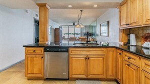 A modern kitchen with wooden cabinets, a stainless steel dishwasher, and a black countertop.