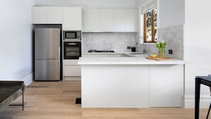 A modern kitchen with white cabinetry, stainless steel appliances, and a marble backsplash. - Brighton Pool Paradise: Designer 3BR Retreat Near Beach & Café Culture (Brighton)
