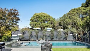 A backyard with a swimming pool, a patio with outdoor furniture, and a wooden fence. - Brighton Pool Paradise: Designer 3BR Retreat Near Beach & Café Culture (Brighton)