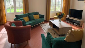 Una sala de estar con un sofá verde, un sillón rojo, una mesa de centro de madera, un televisor y una ventana con cortinas.