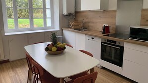 Una cocina moderna con una mesa blanca, sillas rojas, un frutero, un microondas, un lavavajillas y una ventana con vistas a zonas verdes.