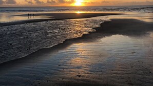 A beach with a sunset, waves, and a few people walking. - Sea view apartment 100m from the beach (Saint-Nic)