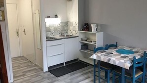 A compact kitchen with white cabinets, a tiled backsplash, and a dining area with blue chairs and a checkered tablecloth. - Sea view apartment 100m from the beach (Saint-Nic)
