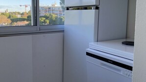 Une cuisine avec une fenêtre, un appareil électroménager blanc et une vue sur des immeubles et des arbres.