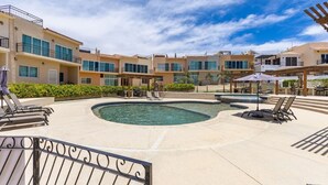A pool area with lounge chairs and umbrellas, surrounded by multi-story buildings with balconies.