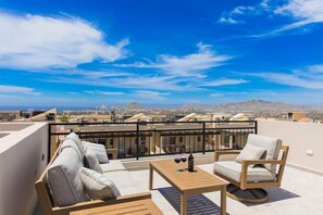 A rooftop terrace with a seating area, a table, and a view of the cityscape.
