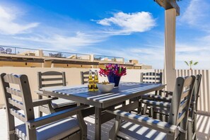 Una mesa con sillas, un florero y dos botellas de cerveza Corona en una terraza con vistas a edificios y cielo despejado.