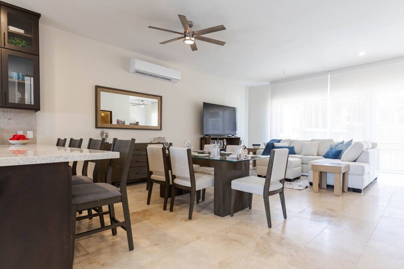 A modern living room with a sofa, a dining area with chairs and a table, a ceiling fan, and a TV.