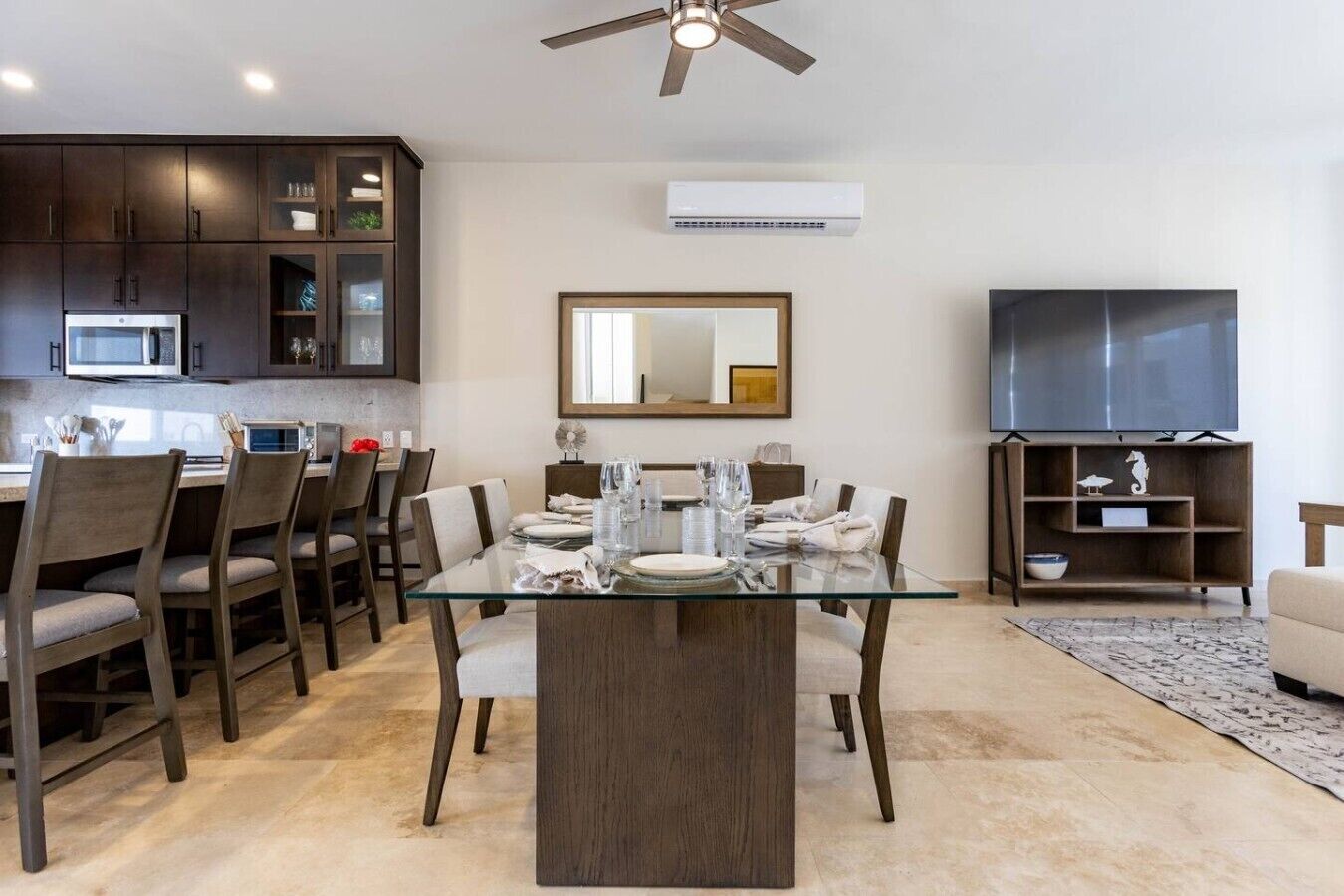 A modern dining area with a glass table, dark wooden chairs, and a ceiling fan.