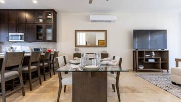 A modern dining area with a glass table, dark wooden chairs, and a ceiling fan.