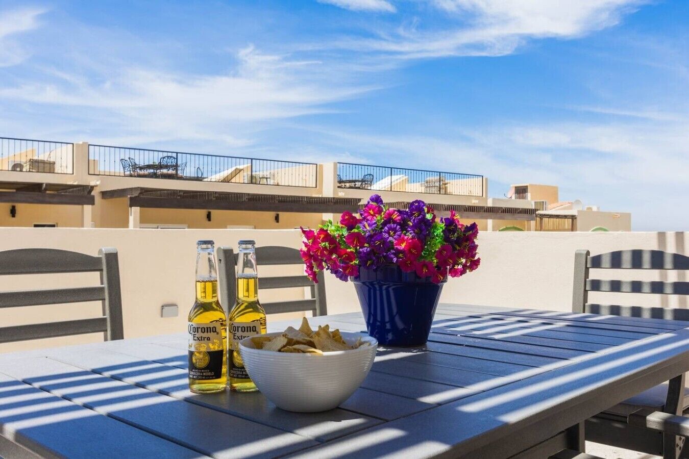 A table with two bottles of Corona Extra beer, a bowl of chips, and a potted plant with purple flowers.