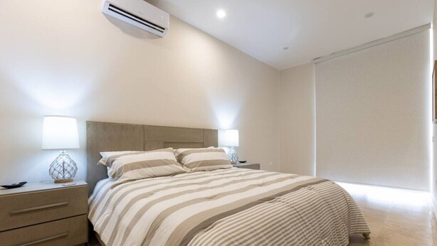 A modern bedroom with a bed, bedside tables, lamps, and an air conditioning unit.