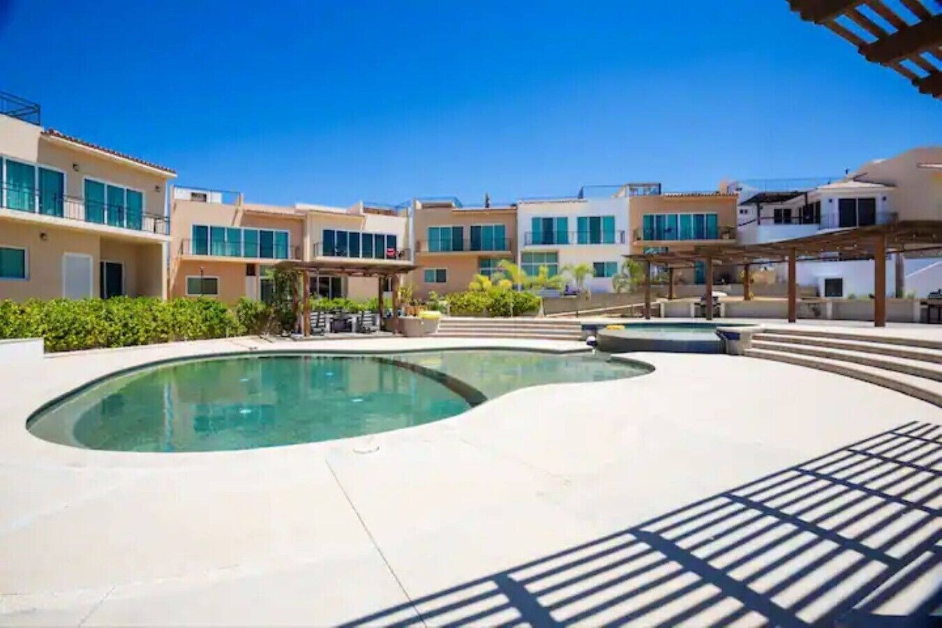 A swimming pool area with a curved design, surrounded by buildings with balconies and a covered seating area.