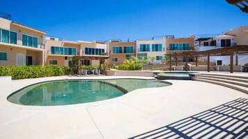 A swimming pool area with a curved design, surrounded by buildings with balconies and a covered seating area.