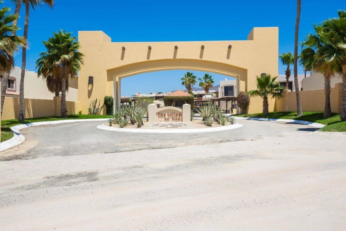 A gated entrance with a curved archway, palm trees, and a clear sky.