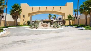 A gated entrance with a curved archway, palm trees, and a clear sky.