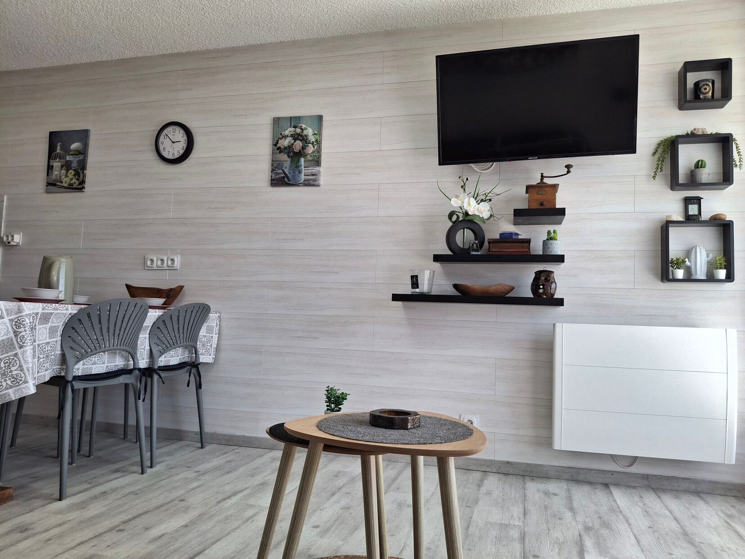 A modern living room with a dining area, a flat-screen TV mounted on the wall, and a white radiator.