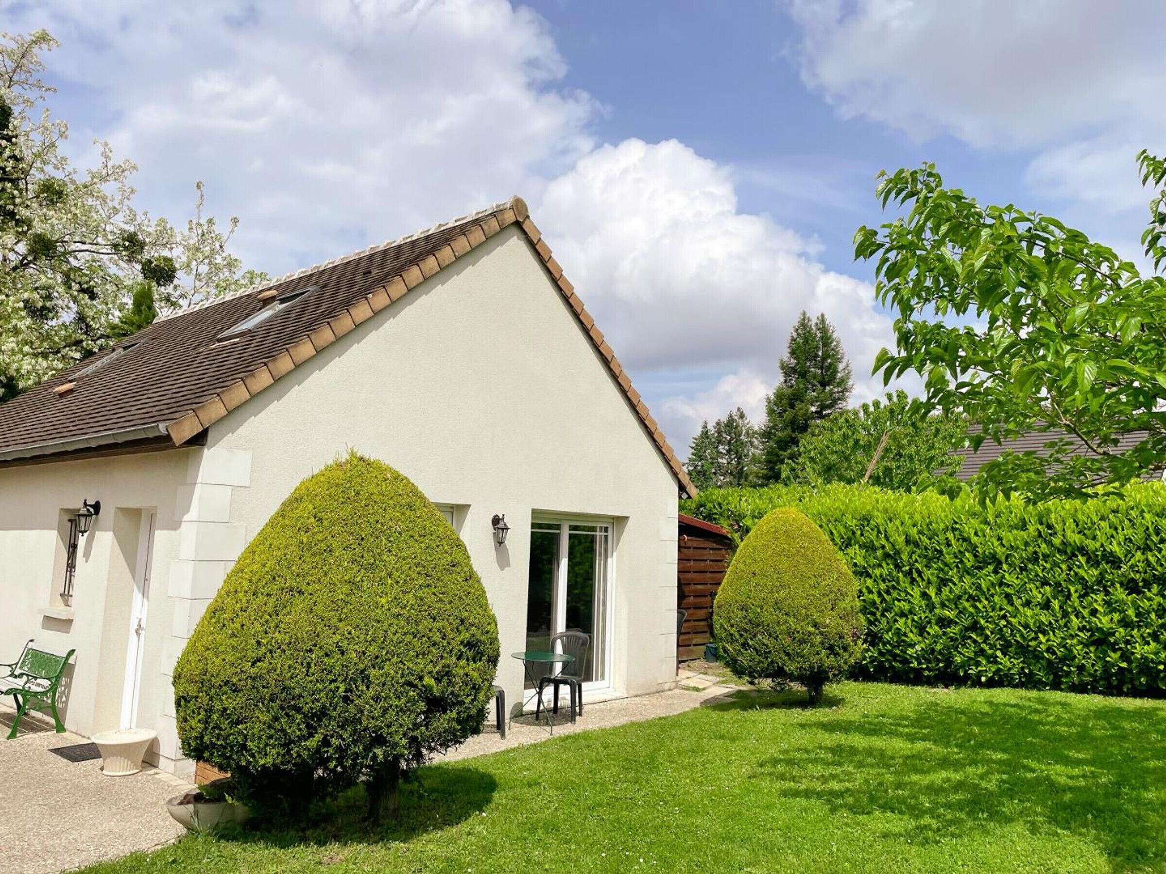 A single-story house with a sloped roof, a small porch with a table and chairs, and a well-maintained lawn.