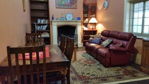 A cozy living room with a fireplace, a leather sofa, a dining table with chairs, and a bookshelf. - Historic Tyford House, close to all amenities (Dongara)