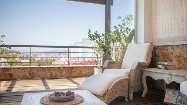 Uma varanda com mobiliário de vime, uma parede de pedra e vista para a cidade.