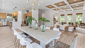 A spacious kitchen with modern appliances, a dining area with a wooden table and white chairs, and a living room with a sofa and coffee table.