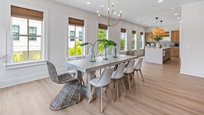 A modern kitchen with white cabinets, a marble countertop, and a dining area with a wooden table and chairs.